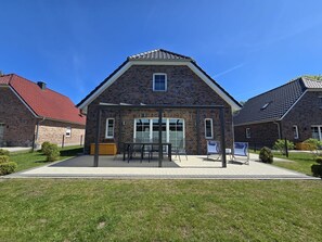 A two-story brick building with a gabled roof, a covered patio area with outdoor seating, and a small garden.