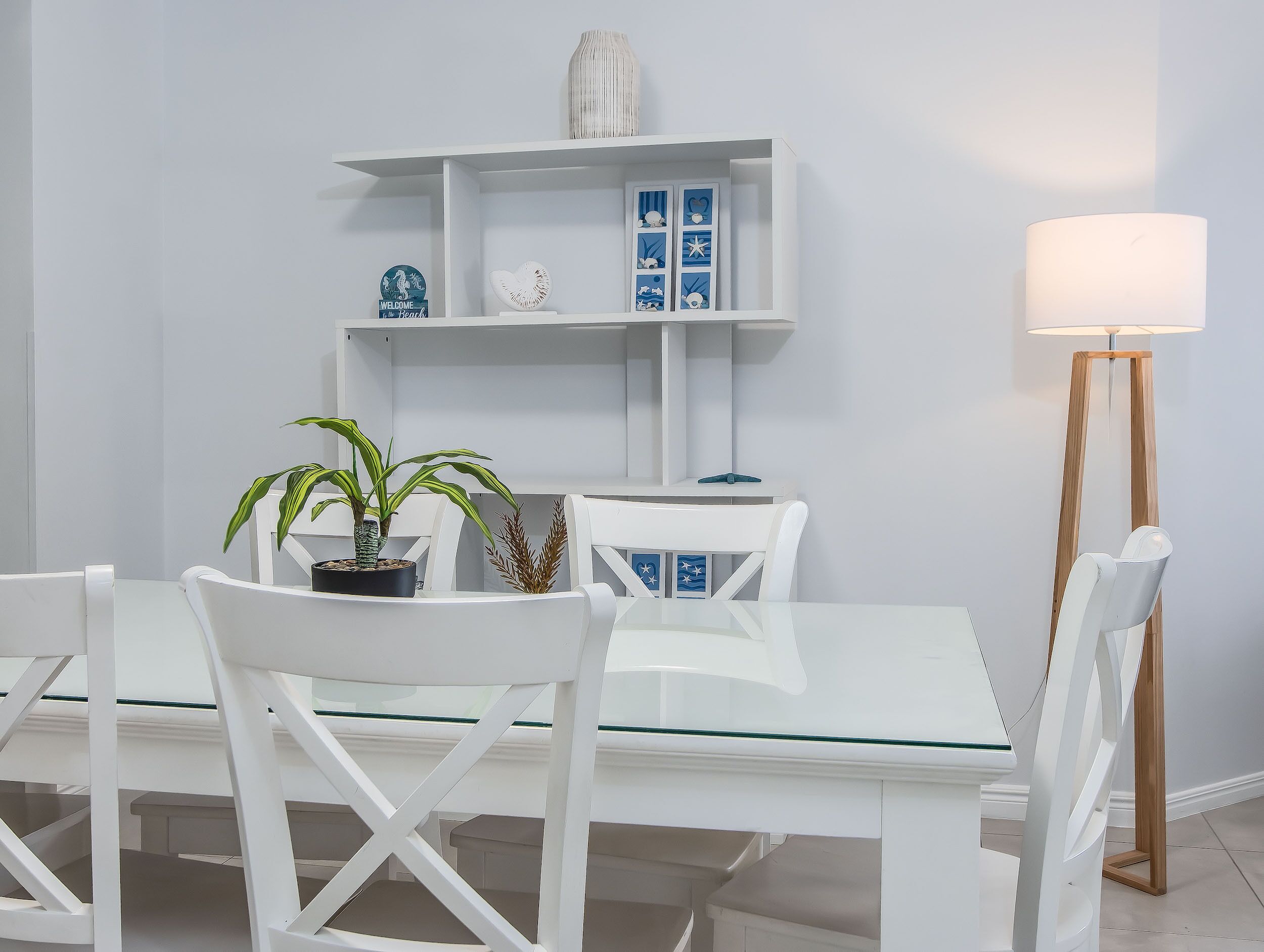 A modern dining area with white furniture, a glass-top table, and a floor lamp.