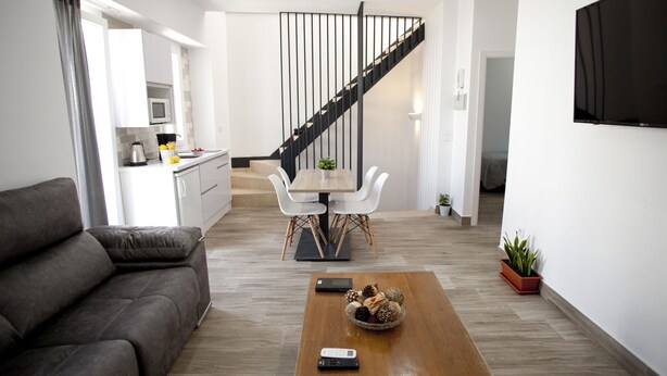A modern living room with a sofa, a coffee table with decorative items, a dining area with a table and chairs, a kitchen in the background, and a staircase. - El Palomar, in Algodonales. (Algodonales)