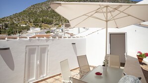 A terrace with a table, chairs, and an umbrella, overlooking a hillside with buildings. - El Palomar, in Algodonales. (Algodonales)