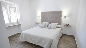 A neatly made bed with a tufted headboard, two bedside tables with lamps, and a window with a plant on the sill. - El Palomar, in Algodonales. (Algodonales)