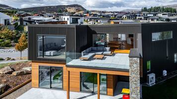 Une maison moderne à deux étages, dotée d’un grand balcon en verre, d’un mur décoratif en pierre et offrant une vue sur un quartier résidentiel.