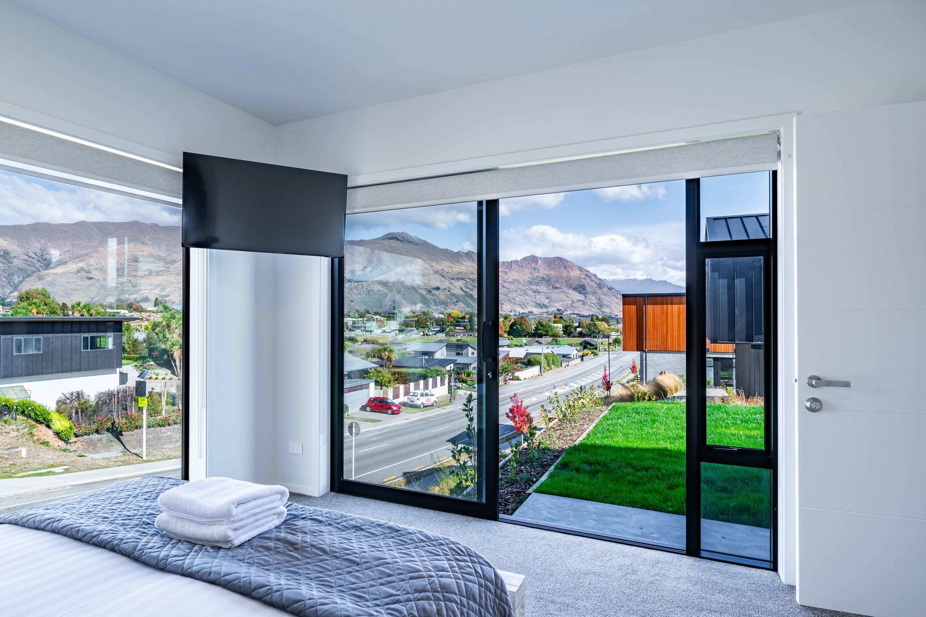 A modern bedroom with a large bed, a view of a cityscape, and a sliding glass door leading to a balcony.