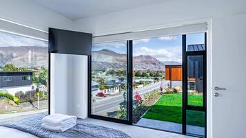 A modern bedroom with a large bed, a view of a cityscape, and a sliding glass door leading to a balcony.