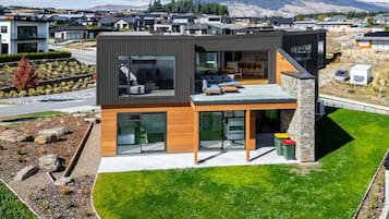A modern two-story house with large windows, a stone fireplace, and a well-maintained lawn.