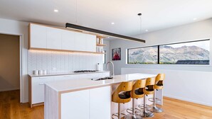 A modern kitchen with a central island, bar stools, and a large window with a mountain view. - Grand Alpine Vista Escape (Wanaka)