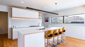 A modern kitchen with a central island, bar stools, and a large window with a mountain view.