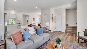 Un salon moderne avec un canapé gris, une table basse et un escalier menant à l’étage supérieur.