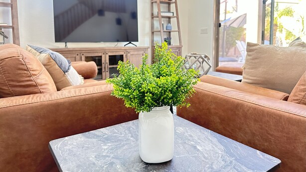 Een woonkamer met een bruine bank, een witte vaas met groene planten, een flatscreen televisie en een houten ladder tegen de muur.