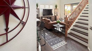 Een ruime woonkamer met een groot muurkompas, een comfortabele bank, een televisie en een trap naar een hoger gelegen niveau.