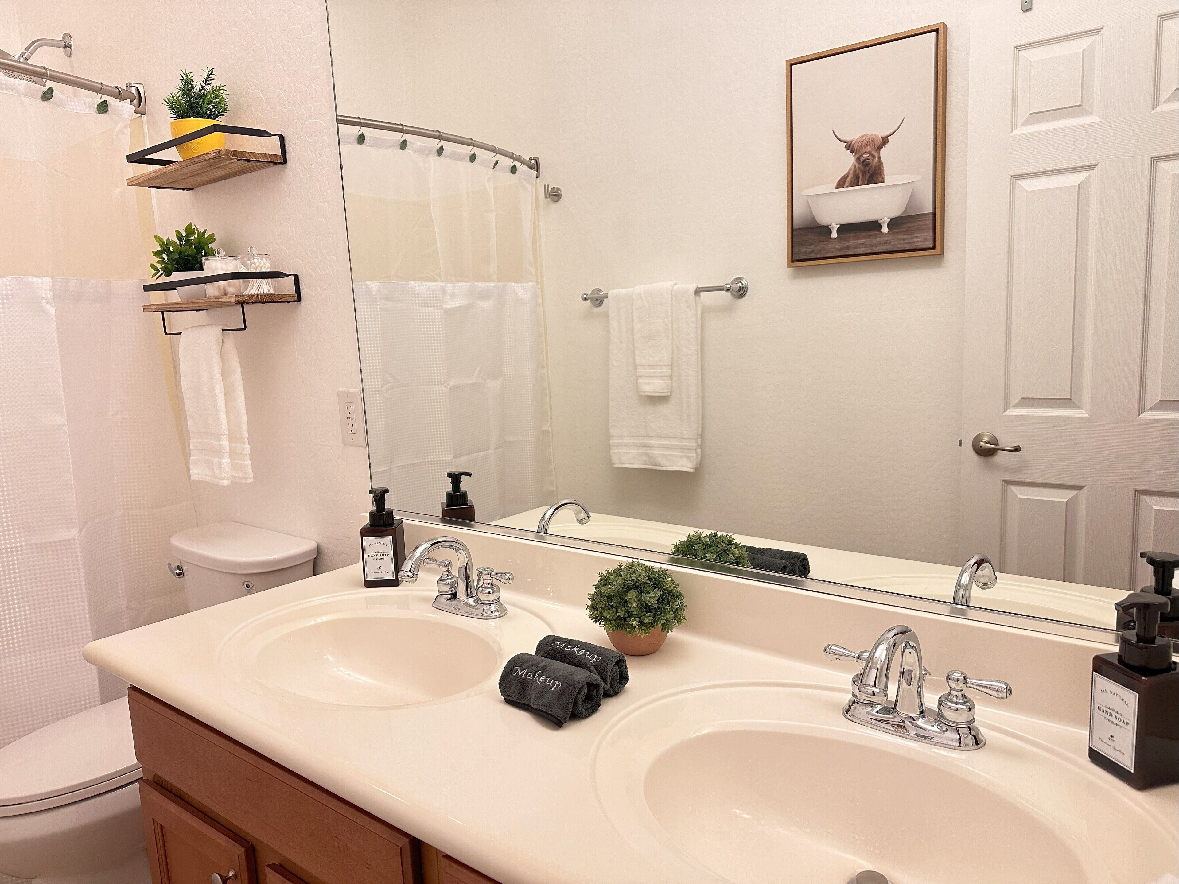 A bathroom with two sinks, a toilet, a shower curtain, a towel rack, a mirror, and a framed picture on the wall.