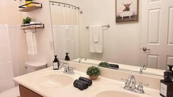 A bathroom with two sinks, a toilet, a shower curtain, a towel rack, a mirror, and a framed picture on the wall.
