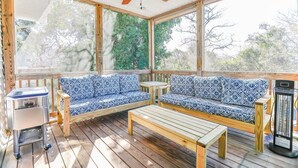 Een overdekt buitengebied met een houten terras, twee blauw gestreepte banken, een houten tafel en een plafondventilator.