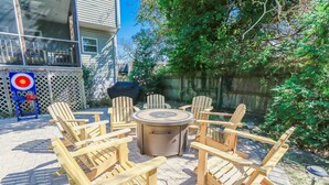 Een terras met houten Adirondack-stoelen en een ronde tafel, omringd door een houten hek en begroeiing.