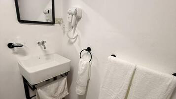 Un baño con un lavamanos blanco, un secador de pelo, un perchero con dos toallas, un espejo y un felpudo a rayas.