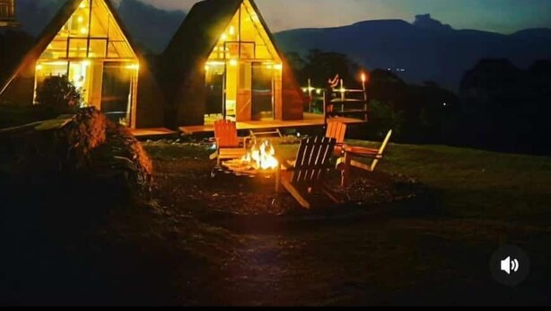 Two illuminated cabins with a fire pit in the foreground, set against a mountainous backdrop. - Chalets Vistas del Poas (Vara Blanca)