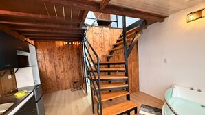A modern kitchen with a wooden staircase, a dining area, and a spa tub. - Chalets Vistas del Poas (Vara Blanca)