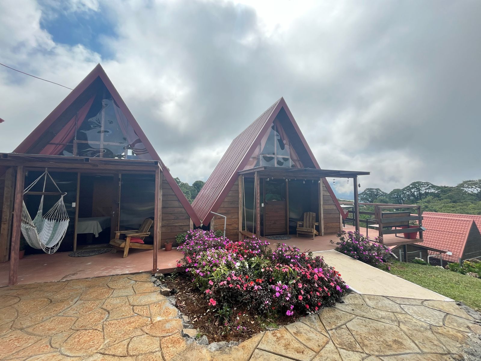 A row of wooden cabins with triangular roofs, a hammock, and a flower bed in front.
