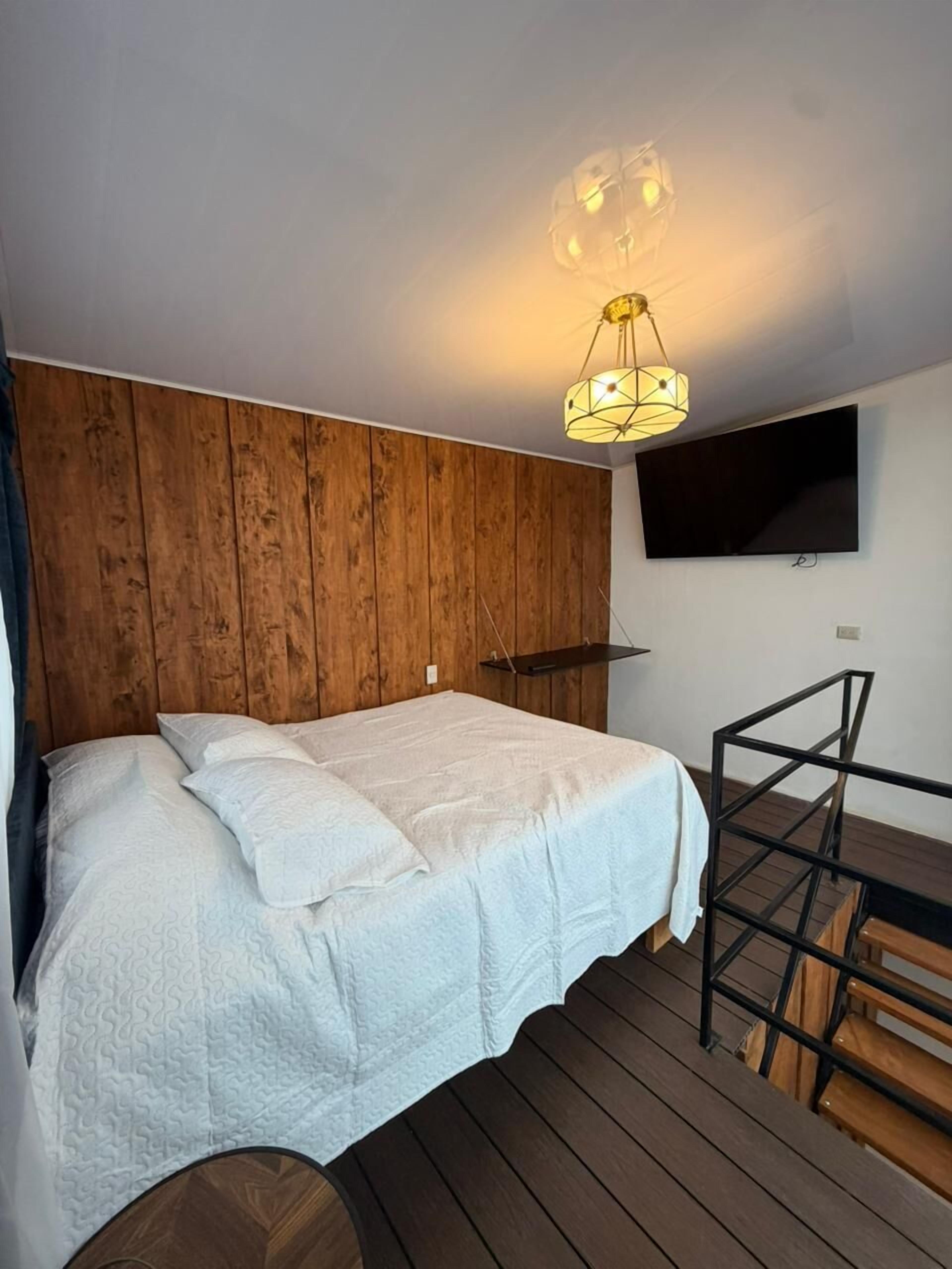 Quarto com uma cama, televisão fixada na parede e piso de madeira.