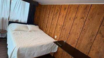 Een slaapkamer met een bed, een hanglamp, houten wanden en een raam met gordijnen.