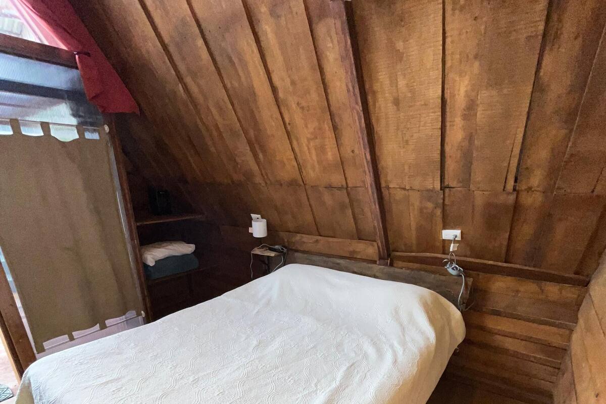 Una habitación de madera con una cama, una mesita y una silla.