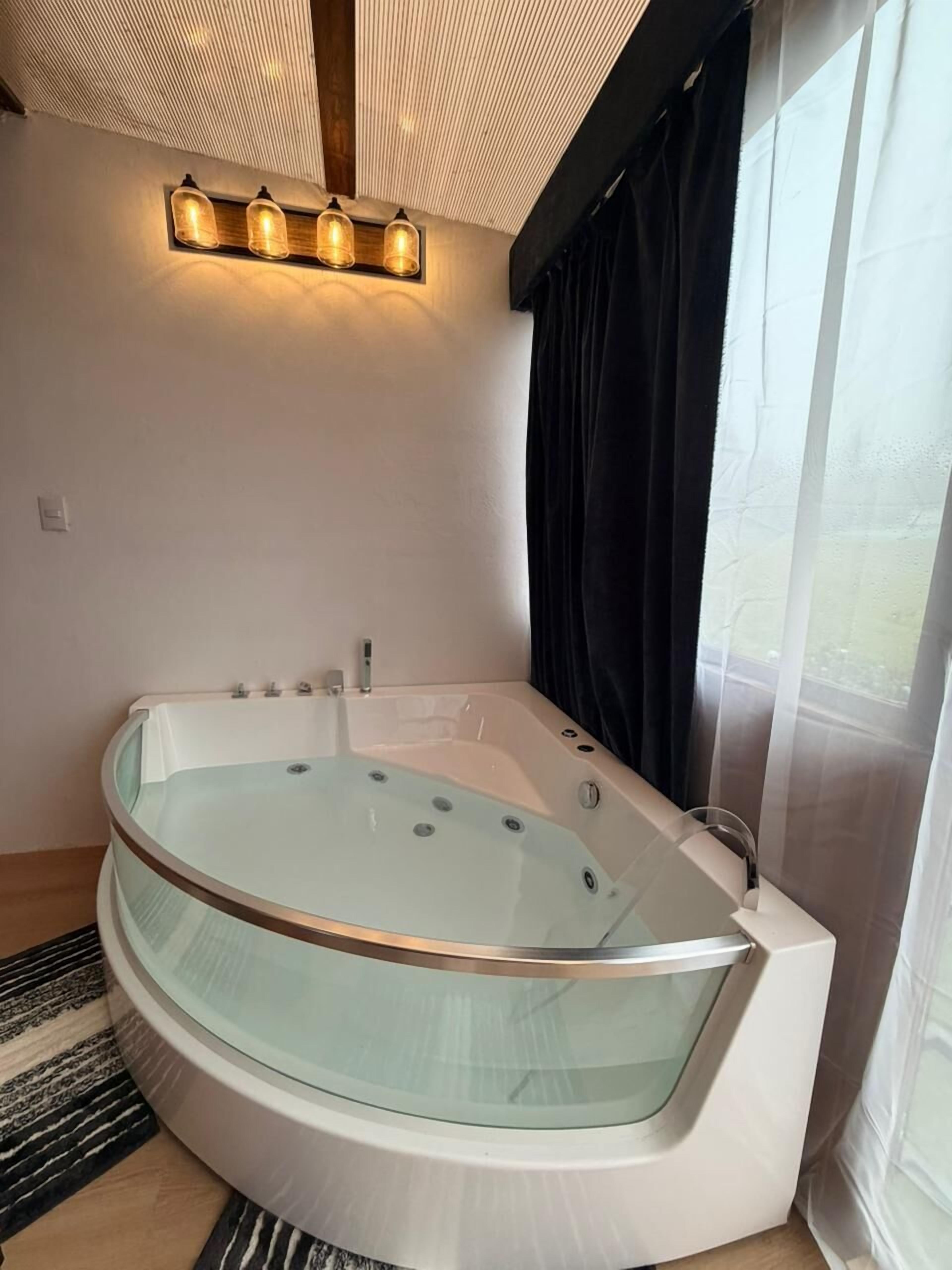 A modern bathroom with a glass-enclosed jacuzzi, a wooden ceiling, and a large window with curtains.
