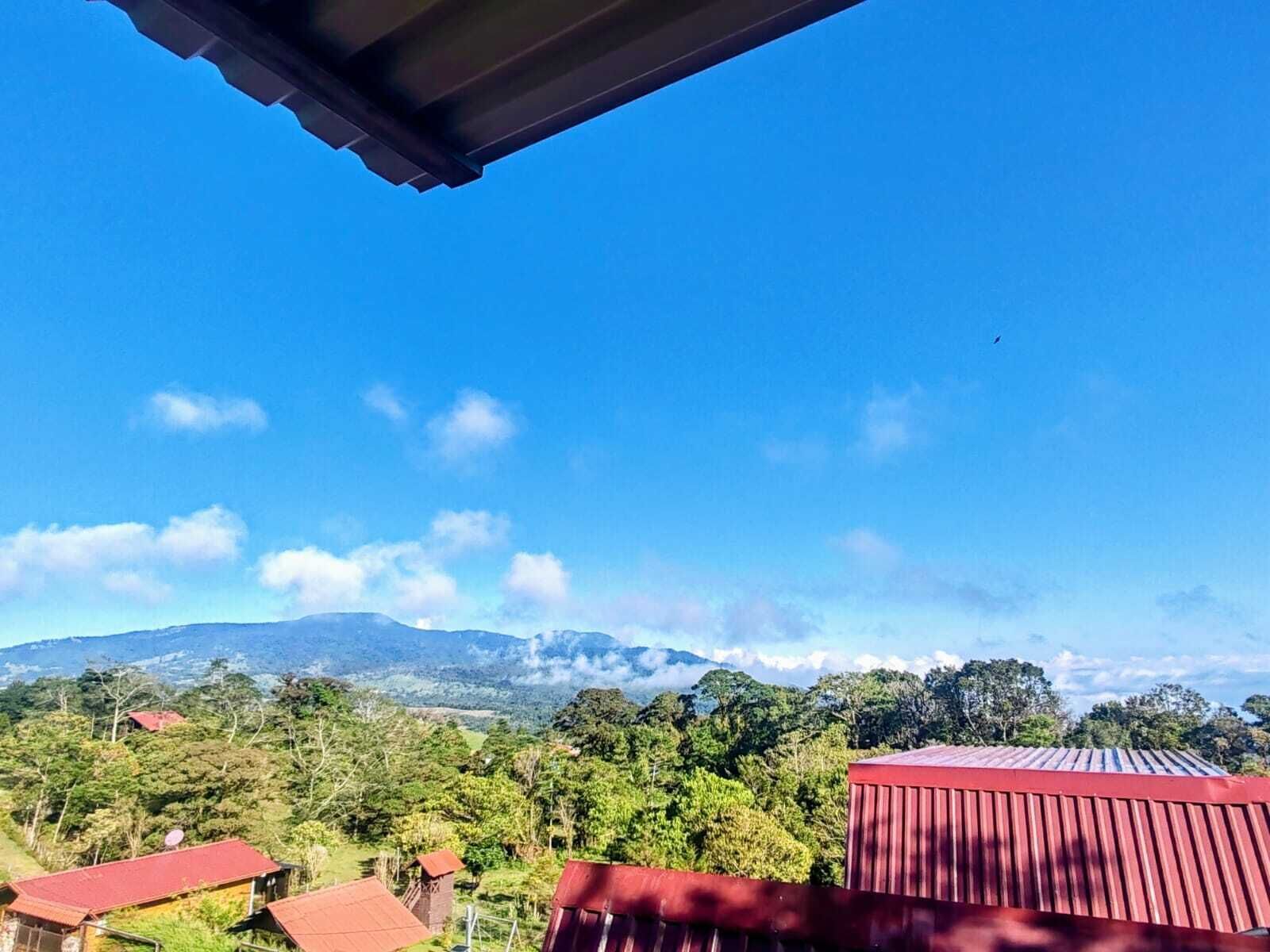 Un paisaje montañoso con cielo despejado, un edificio de techo rojo y una antena parabólica.