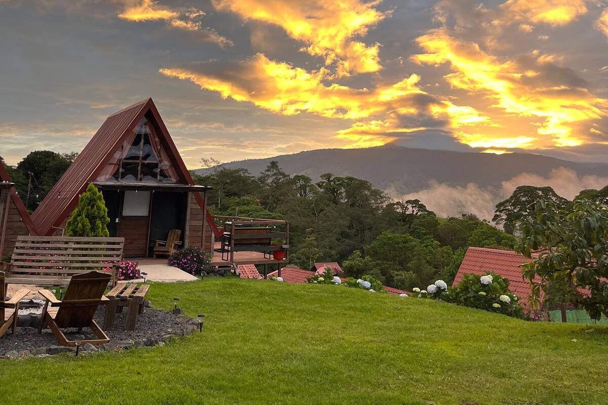 Una cabaña de madera con techo inclinado, una terraza amueblada y vistas del paisaje circundante.