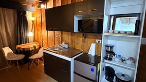 A compact kitchen with a microwave, coffee maker, and a refrigerator. There is a dining area with a table and chairs. - Chalets Vistas del Poas (Vara Blanca)