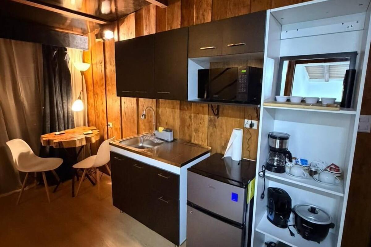 Cocina compacta con microondas, cafetera y refrigerador. Zona de comedor con mesa y sillas.