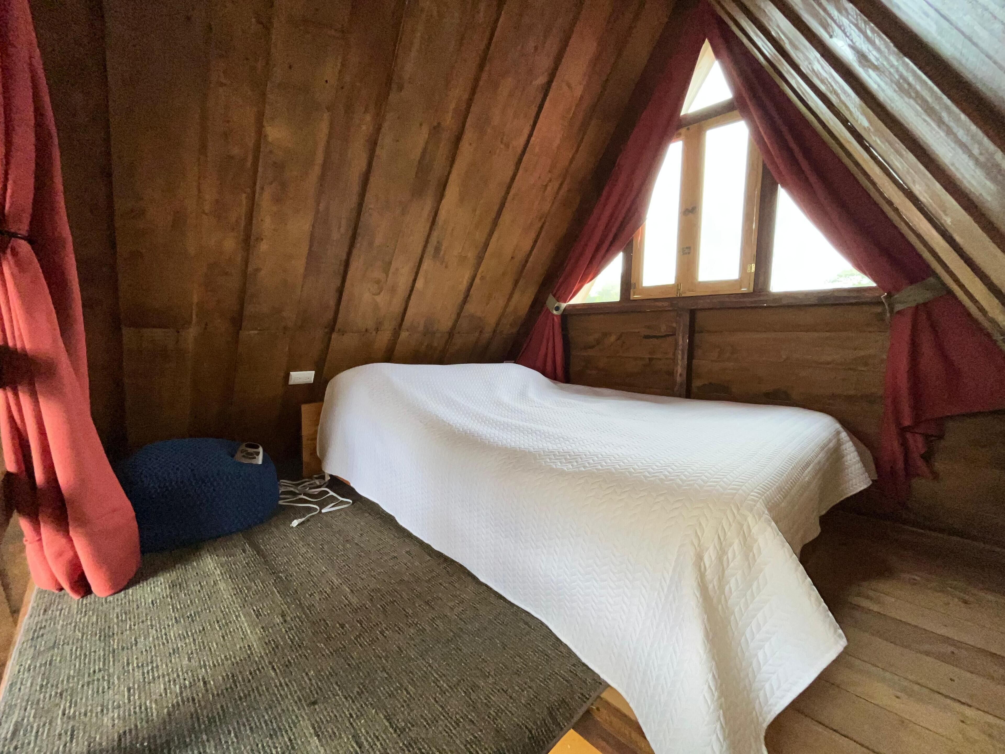 Een knus slaapkamer onder het dak met een enkel bed, een blauw kussen en houten wanden.