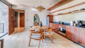 A modern kitchen with wooden cabinets, a round dining table, and a hanging light fixture. - Arthouse Stay with Pool, Gym, & Private Terrace (Tulum)