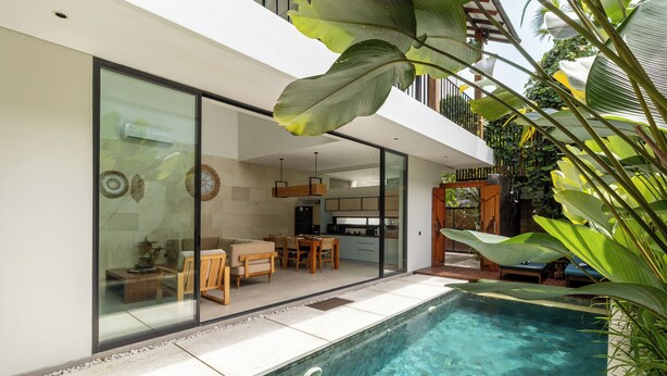 Una casa moderna con un comedor envuelto en vidrio, una cocina y una piscina.