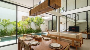 Un comedor moderno con una mesa de madera dispuesta para cuatro personas, un sofá y un amplio ventanal con vistas a una piscina.