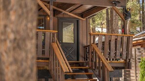 Una escalera de madera que lleva a una puerta con ventanal, rodeada de barandillas de madera y una decoración de oso.