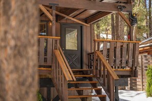 Una escalera de madera que lleva a una puerta con ventanal, rodeada de barandillas de madera y una decoración de oso.