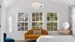 A bedroom with a bed, a sofa, a dresser, a mirror, and three windows. - Modern 4BR w/ Heated Pool | It's Always Sunny (North Myrtle Beach)