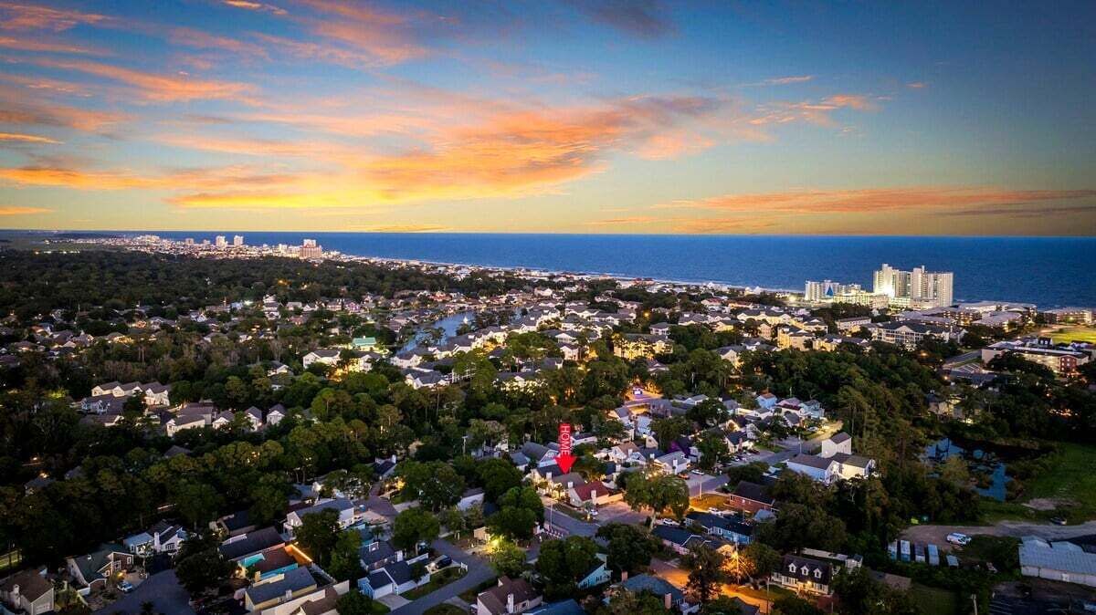 A coastal town with residential buildings, a prominent red arrow pointing to a hotel, and a sunset over the ocean.
