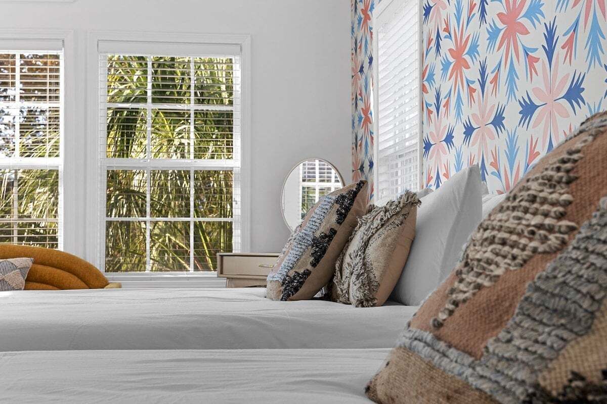 A bedroom with a bed, pillows, a bedside table, and a window with blinds.