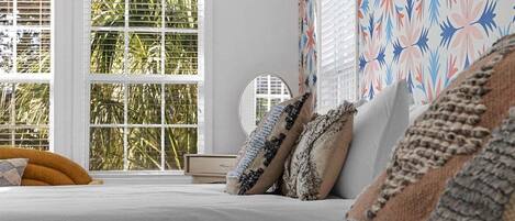 A bedroom with a bed, pillows, a bedside table, and a window with blinds.