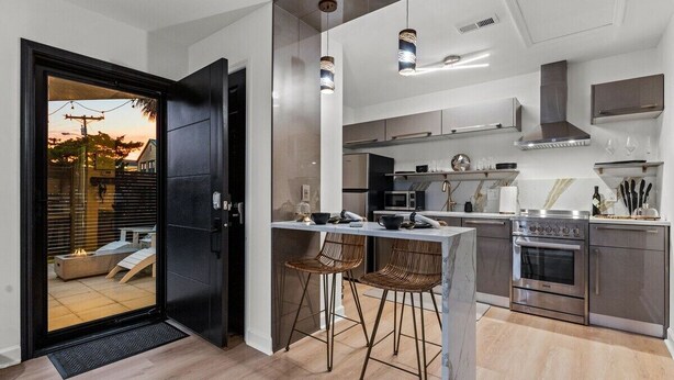 A modern kitchen with a central island, stainless steel appliances, and a black door leading to an outdoor area. - 4BR Lux Townhome w/ Dual Patios and Private Studio (North Myrtle Beach)