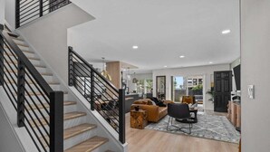 A modern interior with a staircase, a living area with a sofa and chairs, and a dining area. - 4BR Lux Townhome w/ Dual Patios and Private Studio (North Myrtle Beach)
