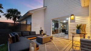 A modern outdoor living area with a sofa, fire pit, and a table with a lamp. - 4BR Lux Townhome w/ Dual Patios and Private Studio (North Myrtle Beach)