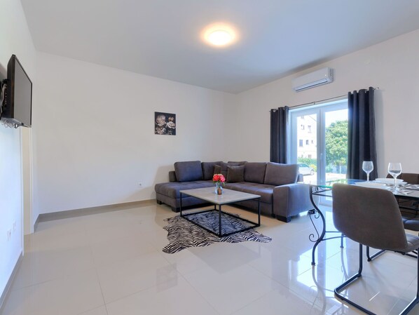 Uma sala de estar moderna com sofá, mesa de centro e um espaço de jantar com cadeiras e mesa de vidro.