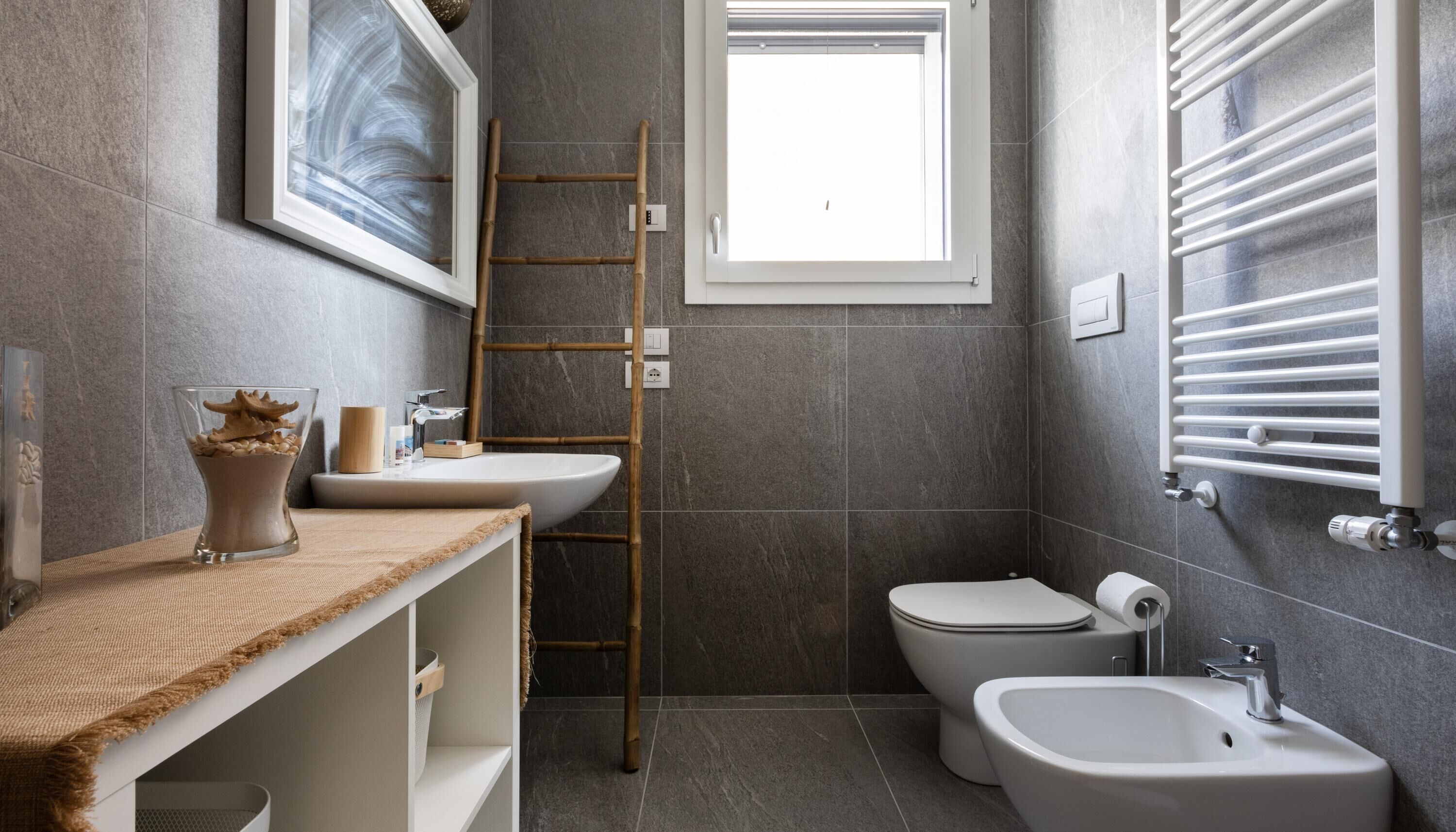 A modern bathroom with a large window, a bidet, a sink, and a toilet.