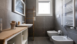 A modern bathroom with a large window, a bidet, a sink, and a toilet.