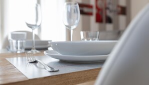 A dining table set with white plates, a fork, and two wine glasses.