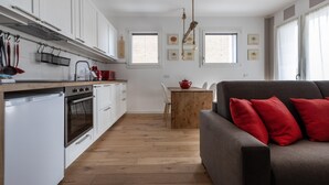 A modern kitchen with white cabinets, a wooden countertop, and a built-in oven. There is a dining area with a wooden table and chairs, and a gray sofa with red cushions. - Italianway - Piranesi 18 B int C 345 - City View (Milan)