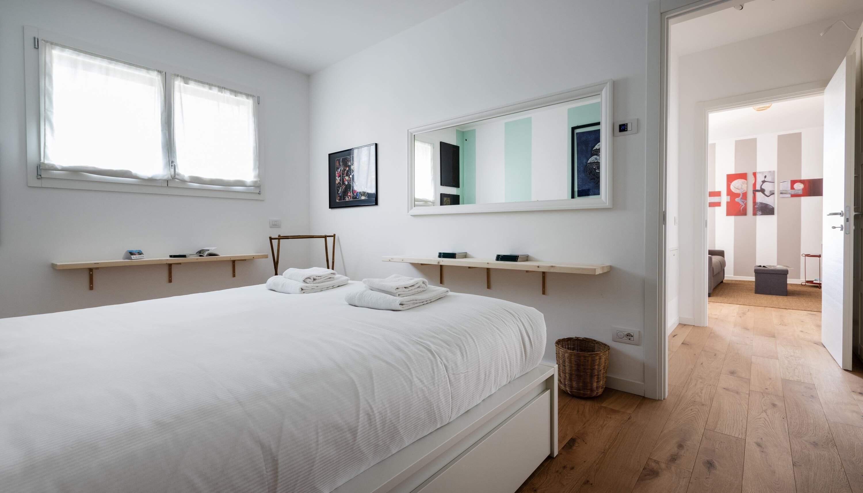 A modern bedroom with a large bed, two bedside tables, a mirror, and a view into another room.
