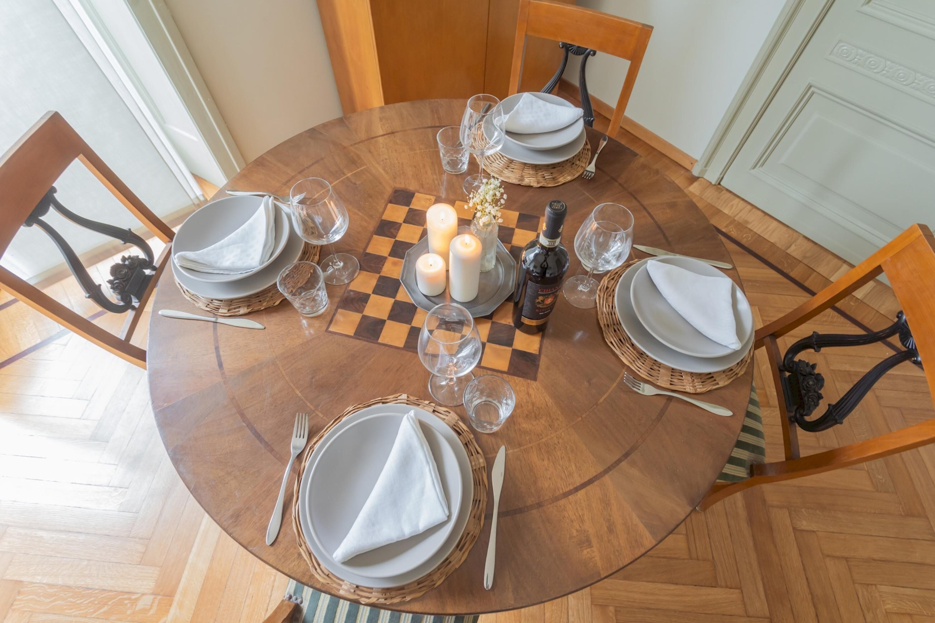 A round dining table with a checkered tablecloth, white napkins, and candles.